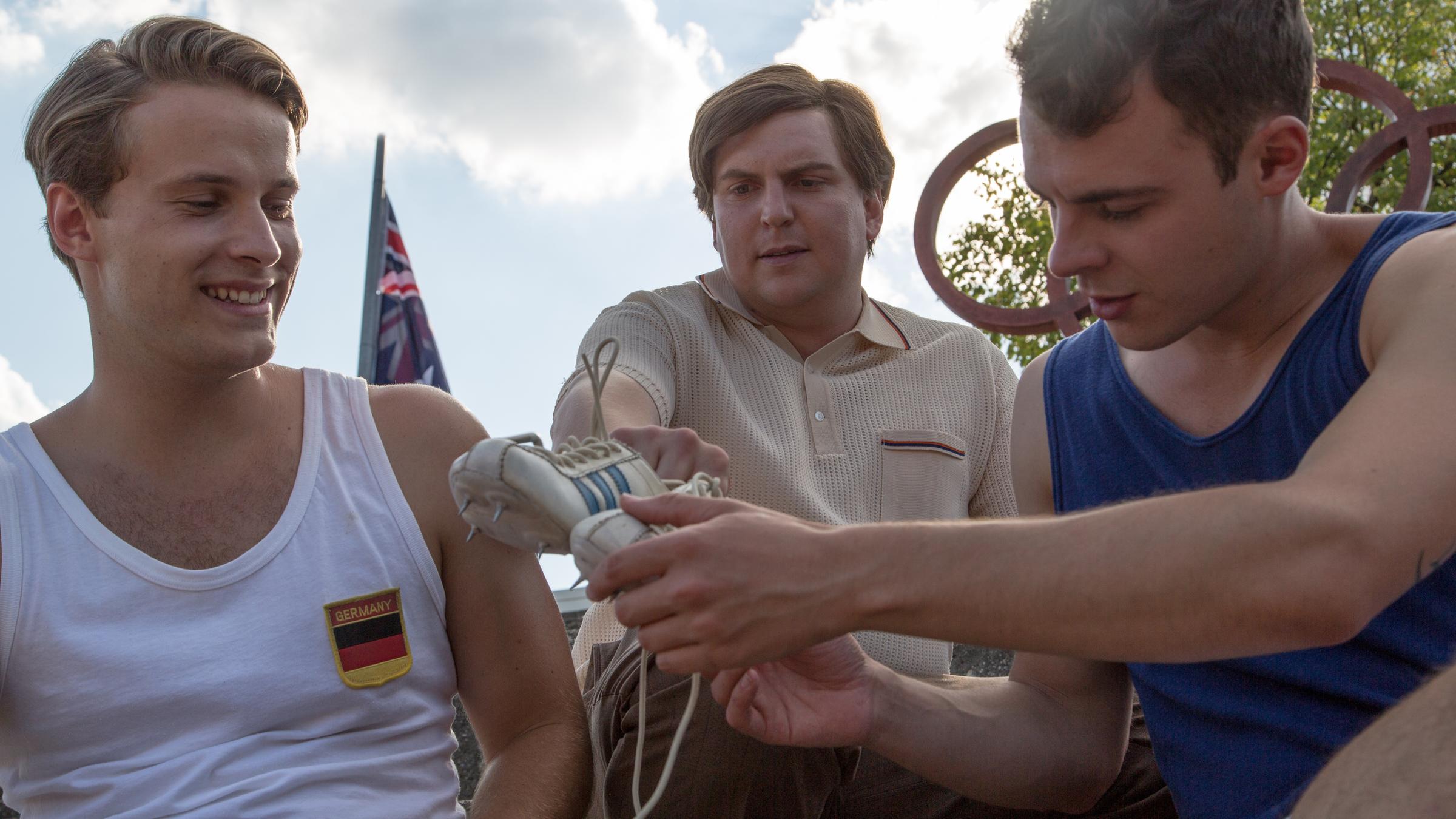 "Deutschlands große Clans - Die Adidas-Story":  Horst Dassler (Franz-Xaver Zeller) überlässt zwei jungen Leichtathleten (Nicolas Wolf, Philipp Liebl) ein Paar Schuhe.