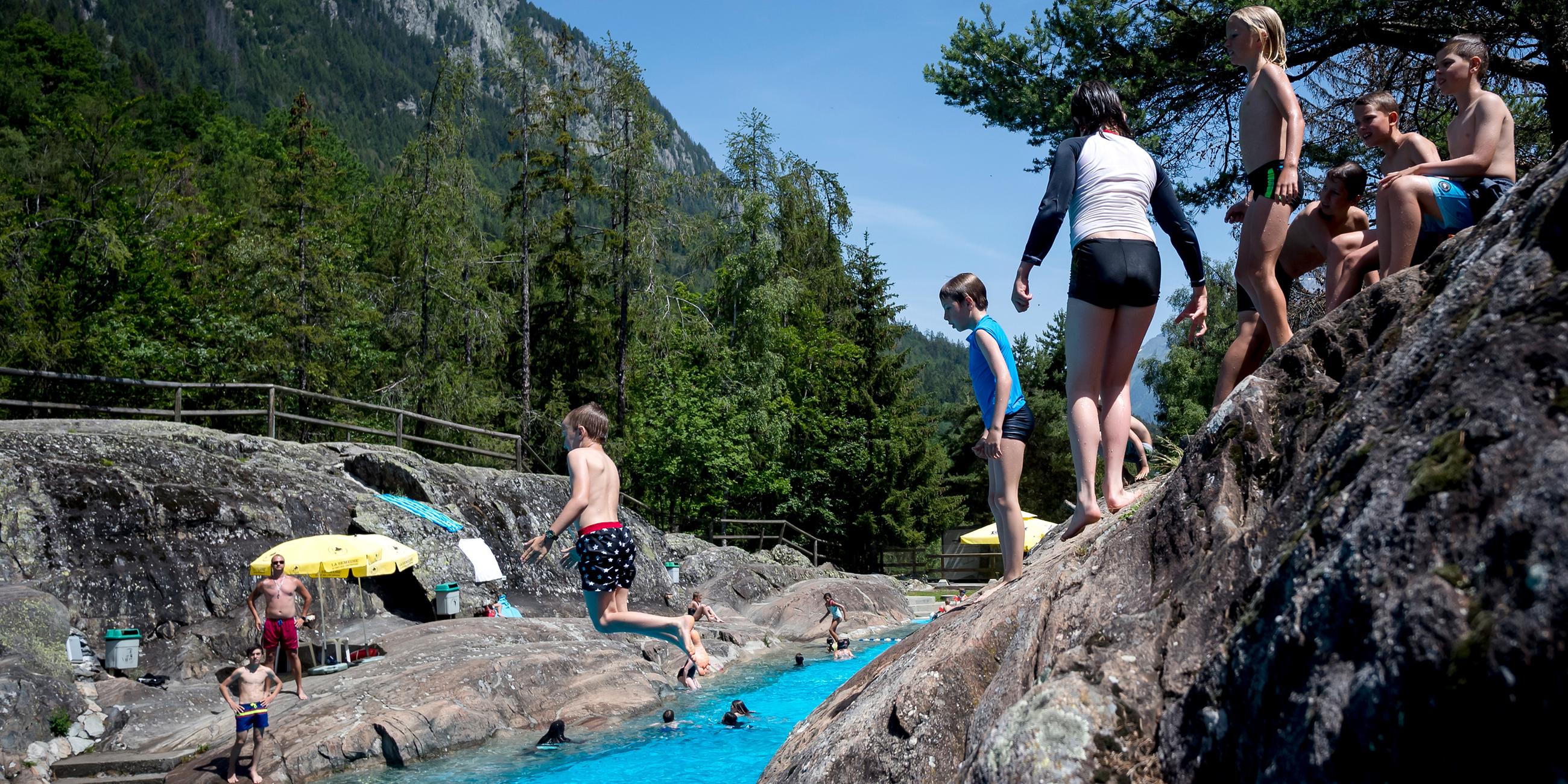 Besucher des alpinen Naturschwimmbads springen ist das Wasser am 25.06.2019 in Les Marecottes (Schweiz)