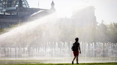 Eine Passantin erfrischt sich in einer Wasserfontäne vor dem Reichstag am 25.06.2019 in Berlin