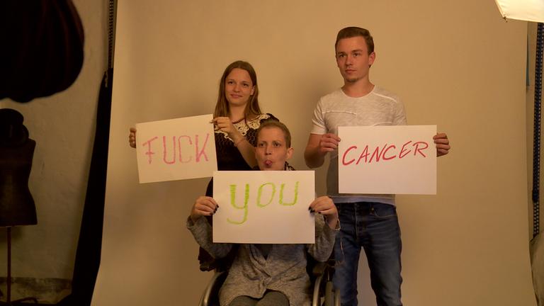  "37° - Ich sterbe, wie ich will: Entscheidung am Ende des Lebens": Drei Personen mit Transparenten in der Hand, auf denen "Fuck you cancer" geschrieben steht.