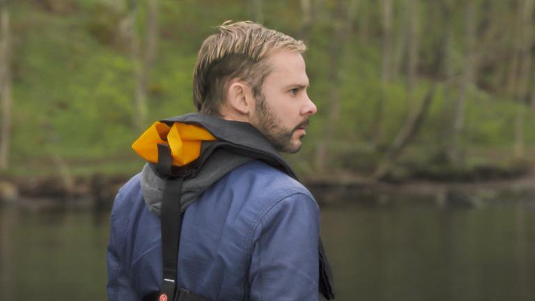 "100 Code - Wintermädchen": Detective Tommy Conley (Dominic Monaghan) steht mit Schwimmweste an einem See und schaut über die Schulter.