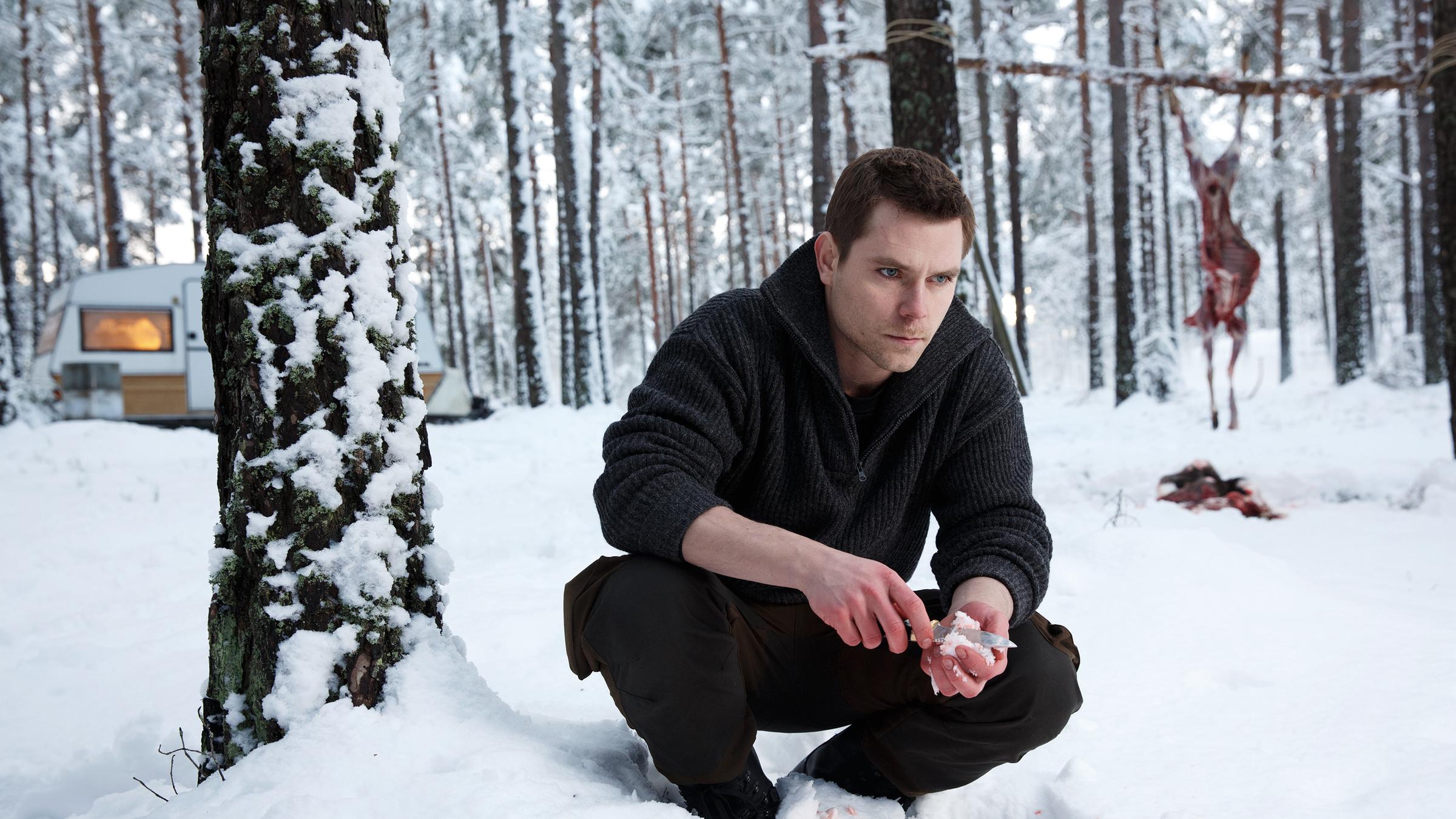 "Modus - Der Mörder in uns (1)":  Richard Forrester (Marek Oravec) hockt im Wald im Schnee. Im Hintergrund hängt ein ausgeweidetes Re