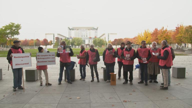 "ZDFzoom: Das Rentendebakel": Eine Gruppe Rentner mit roten Streik-Jacken demonstriert mit Transparenten vor Berliner Ministerium.