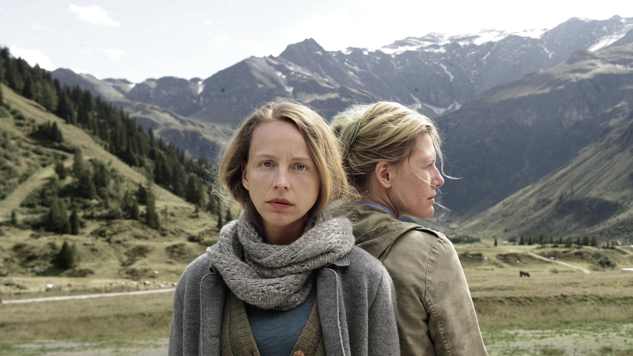 "Das Dorf des Schweigens": Eva (Petra Schmidt-Schaller) und Lydia (Ina Weisse) stehen Rücke an Rücken vor einer Bergkulisse.