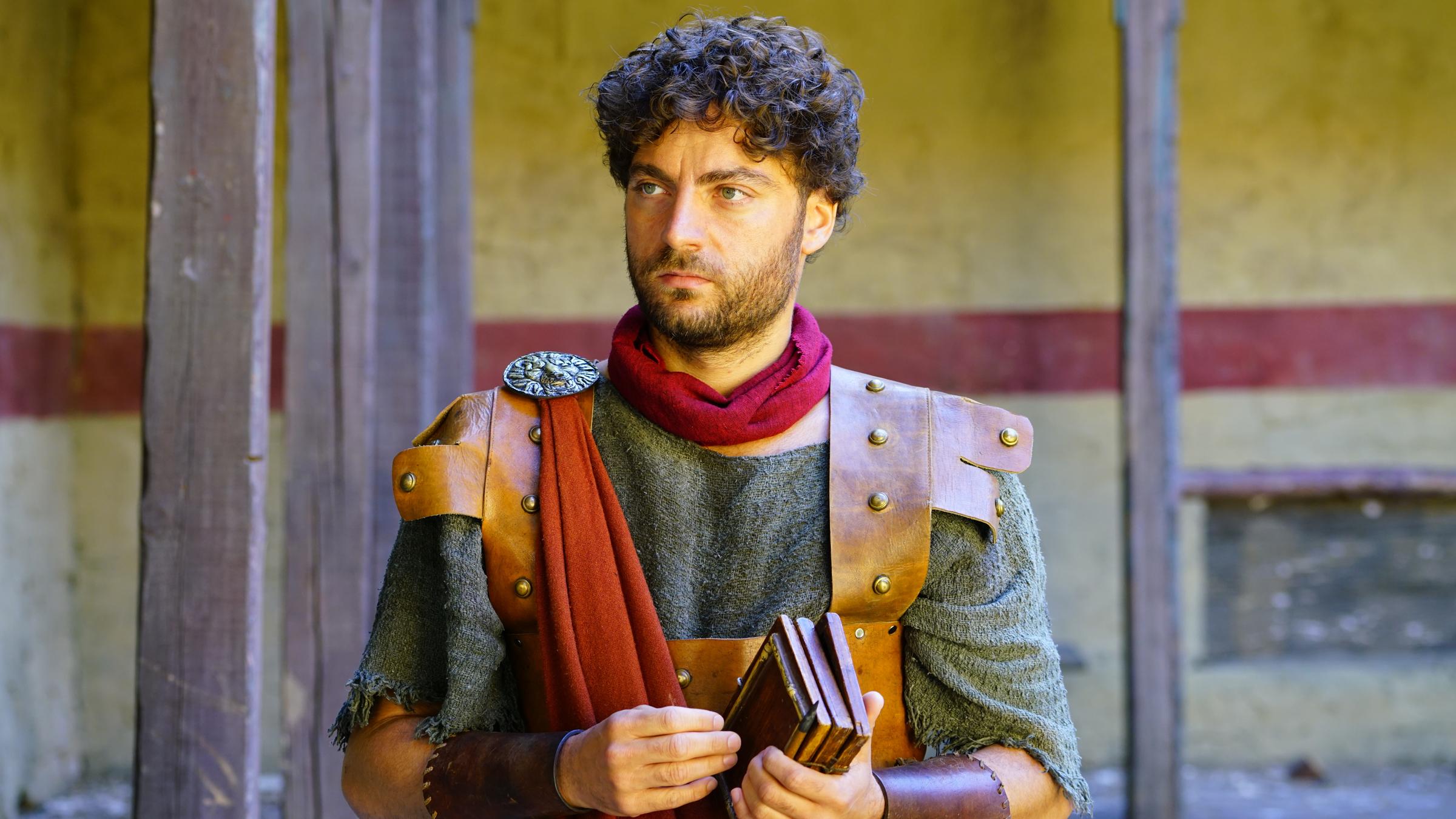 "Terra X - Ein Tag im Alten Rom": Feuerwehrmann Quintus (Timur Isik) in Uniform, hält Notiztafeln in den Händen.