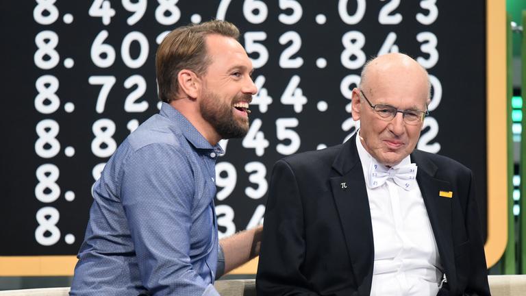 "Deutschlands Superhirn": Steven Gätjen und Kandidat Willem Boumann. Im Hintergrund eine  Schiefertafel mit Zahlen.