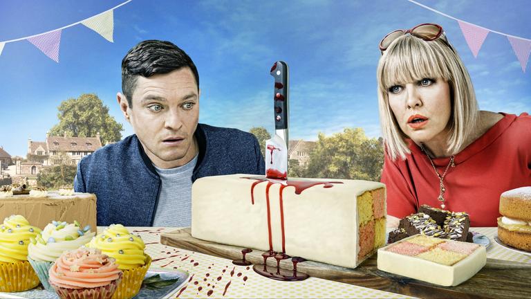 "Agatha Raisin - Und der tote Richer": Agatha Raisin (Ashley Jensen) und Roy Silver (Mathew Horne) stehen hinter einem Tisch, der mit Kuchen und Muffins gedeckt ist. Sie blicken entsetzt auf einen der Kuchen, in dem ein blutiges Messer steckt.