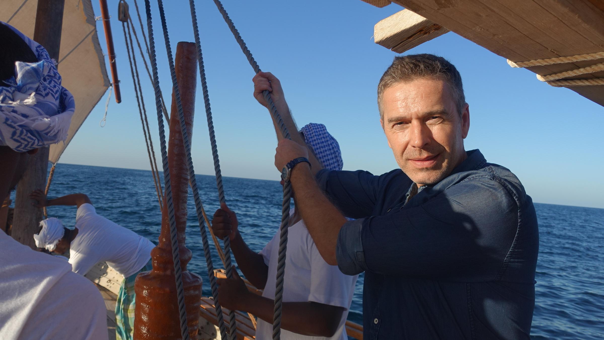 "Terra X: Faszination Erde - mit Dirk Steffens: Arabien - Zauberreich zwischen den Welten": Dirk Steffens steht auf einem Segelschiff und hält ein gespanntes Seil fest, während er in die Kamera blickt. Neben ihm stehen weitere Männer. Im Hintergrund ist das offene Meer zu sehen.