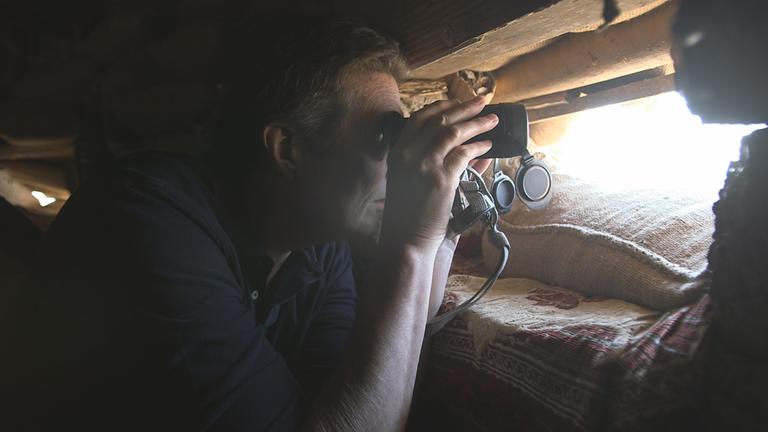"Krieg gegen den IS - Die Welt und der islamistische Terror": Reporter Martin Smith beobachtet mit dem Fernglas die Frontlinie von einer geschützten Stellung aus.