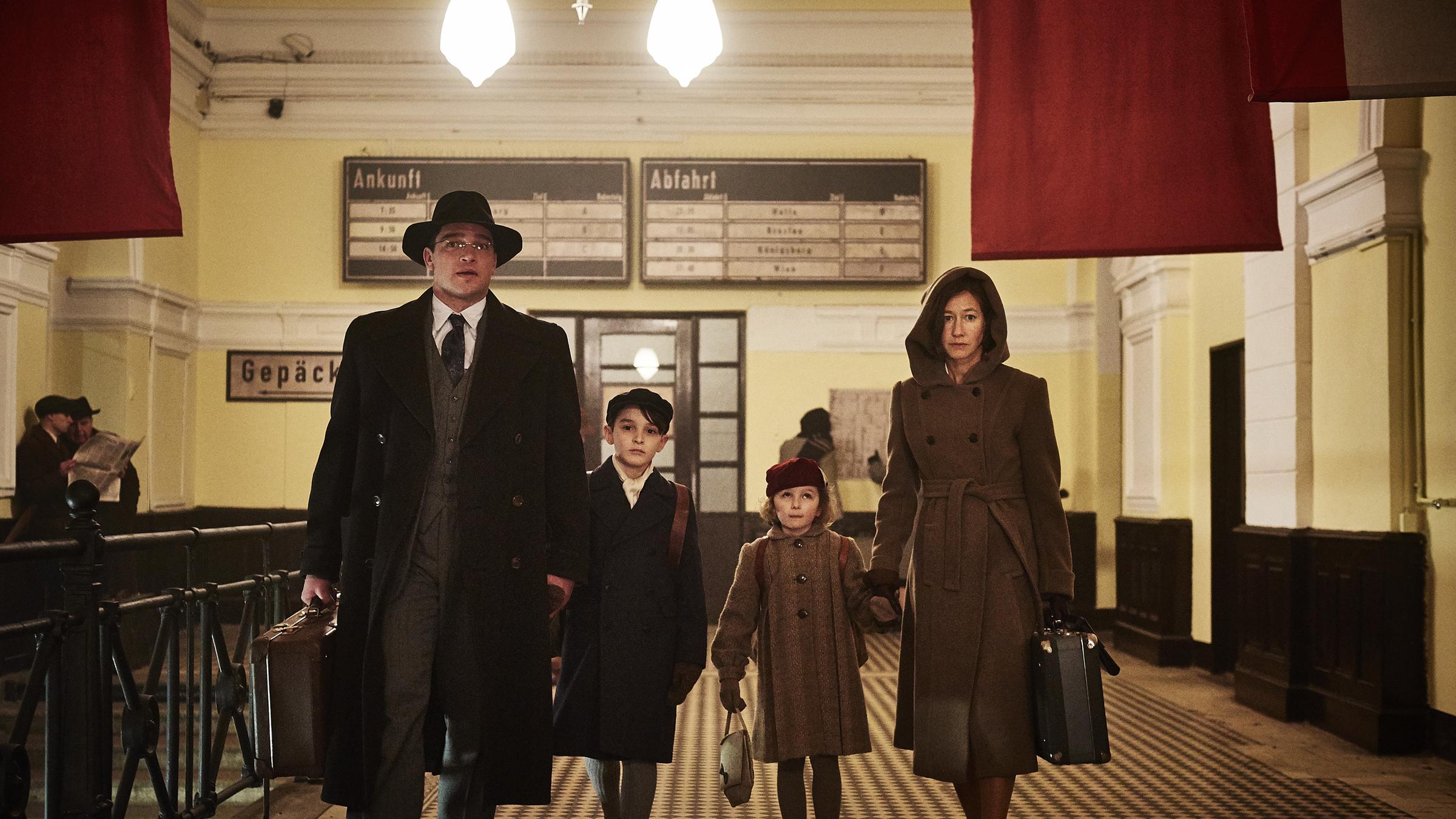 "Landgericht - Familiengeschichte (1)": Richard (Ronald Zehrfeld), Claire (Johanna Wokalek) und ihre Kinder Georg (Moritz Hoyer) und Selma Kornitzer (Lisa Marie Trense) laufen durch eine Bahnhofshalle. Die Eltern tragen jeweils einen kleinen Koffer und wirken besorgt.