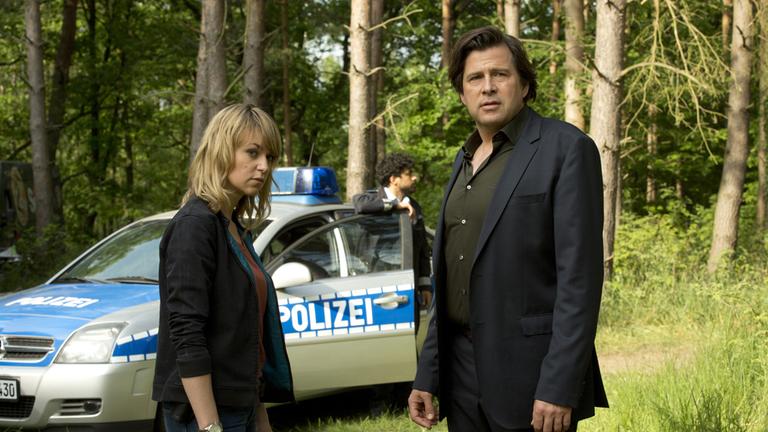 "Kommissarin Heller - Verdeckte Spuren": Kommissarin Heller (Lisa Wagner) und Kommissar Verhoeven (Hans-Jochen Wagner) stehen nebeneinander im Wald. Im Hintergrund ist ein Polizeiwagen zu sehen.