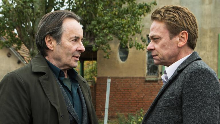 "Ein Kommissar kehrt zurück": Günther Kovak (Uwe Kockisch) und Prof. Michael Adam (Sylvester Groth) stehen sich gegenüber und schauen sich mit ernstem Blick an.