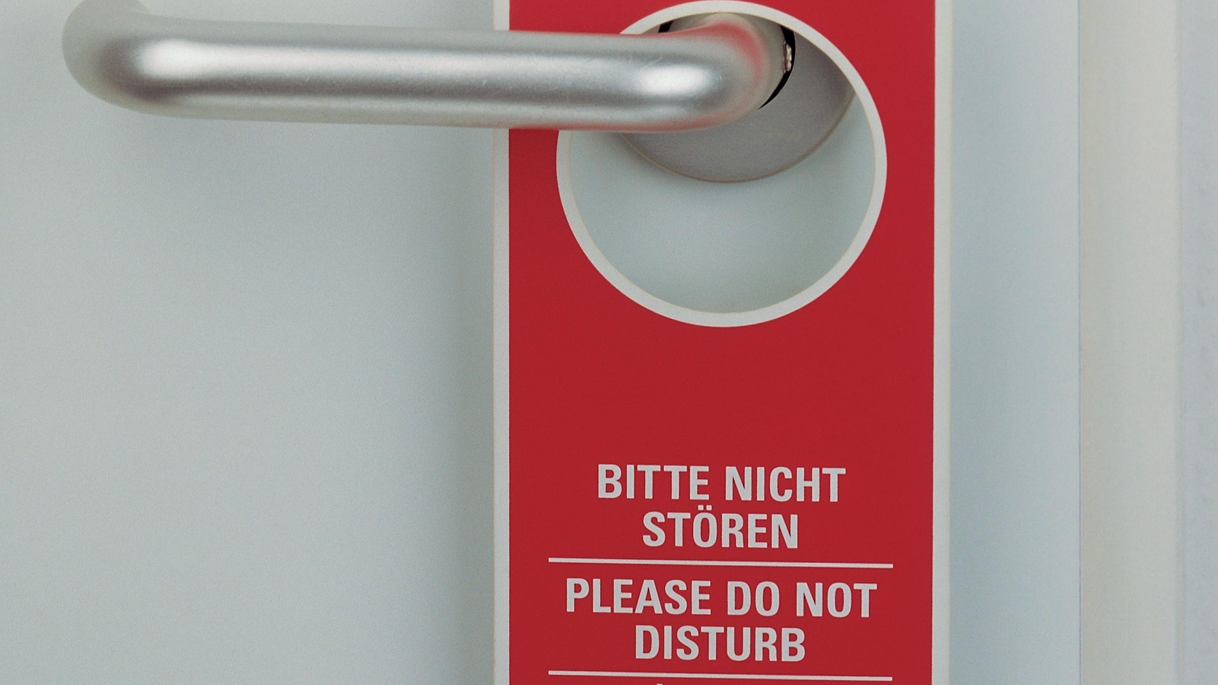 An einer Türklinke hängt ein Schild auf dem steht "bitte nicht stören" und auf englisch "do not disturb"