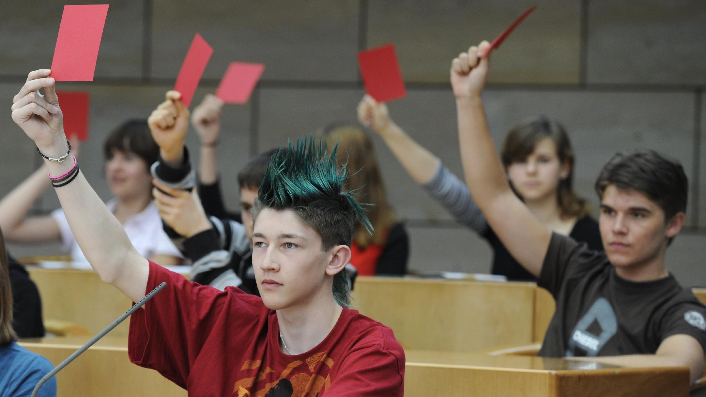 Kinder und Jugendliche halten bei einer Abstimmung Karten nach oben.