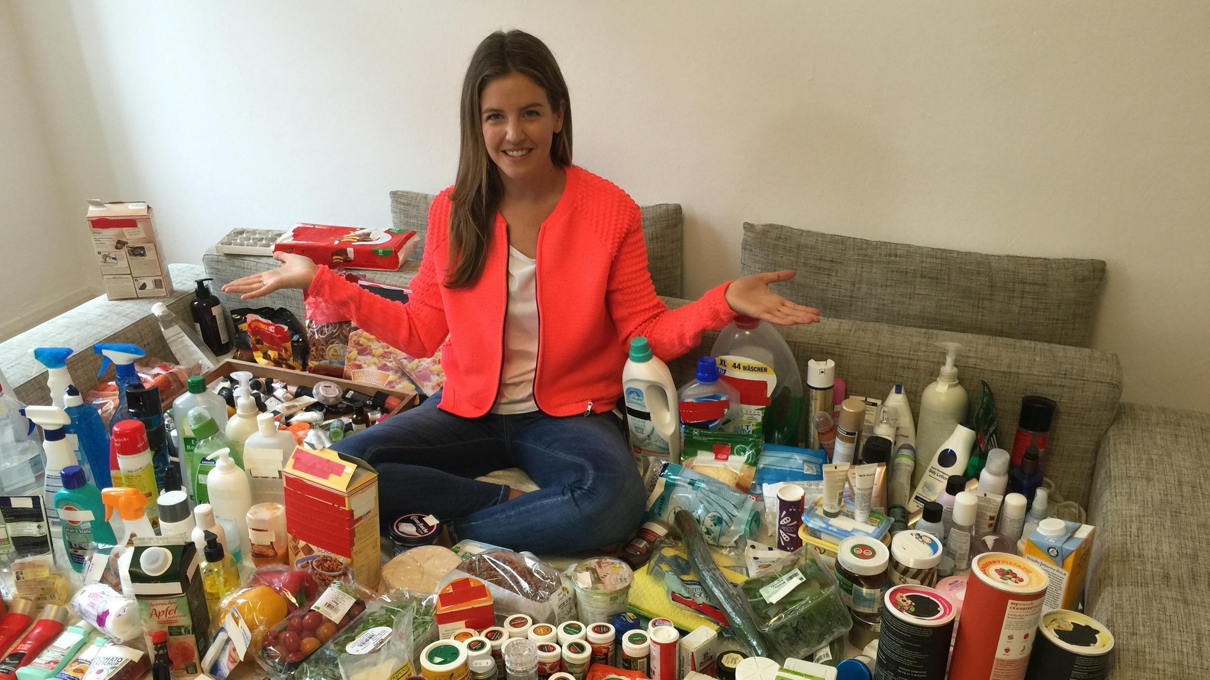 logo! extra: logo! Moderatorin Jennifer Sieglar sitzt auf einem Sofa. Um sie herum lauter in Plastik verpackte Produkte.