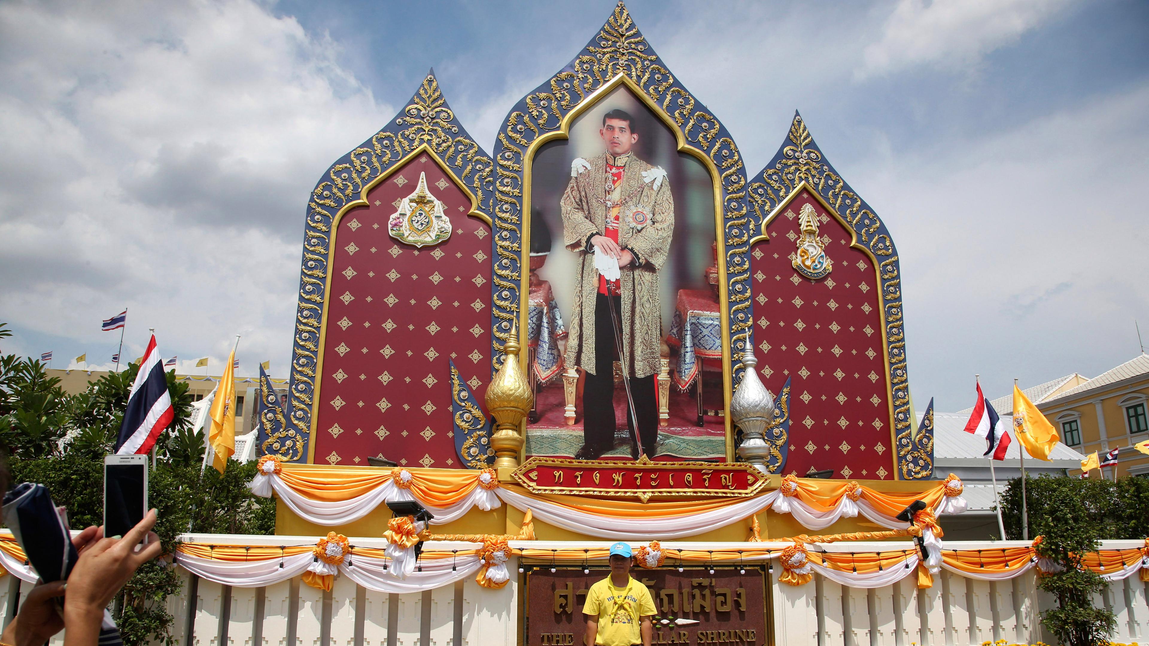 Ein Mann lässt sich am Großen Palast vor einem überlebensgroßen Bild des neuen Königs fotografieren.