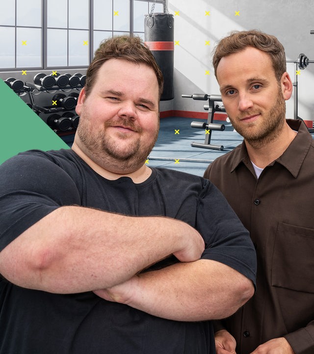 Thorsten Prix und Dr. Leon Windscheid stehen nebeneinander in einem Fitnessstudio. Thorsten Prix verschränkt die Arme und lächelt selbstbewusst, während Dr. Leon Windscheid ruhig in die Kamera blickt. Im Hintergrund sind Hantelbänke und Fitnessgeräte zu sehen.
