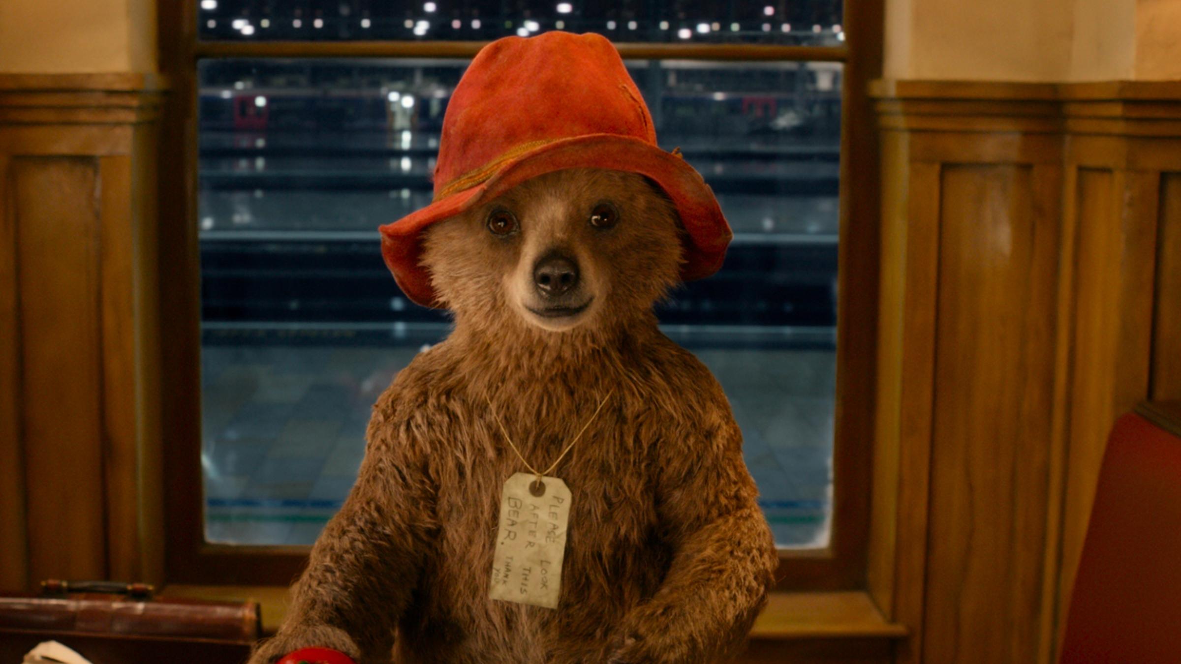 "Paddington": Der kleine Bär Paddington sitzt mit Hut und kleinem Schild um den Hals im Bahnhofs-Café.