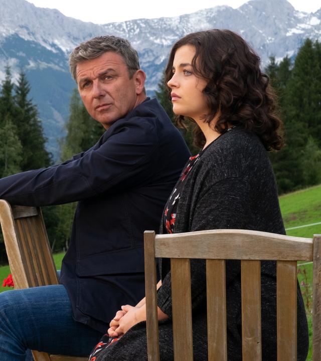 "Der Bergdoktor: Bittere Tränen": Martin Gruber (Hans Sigl) sitzt mit ernster Miene neben Lilli (Ronja Forcher) im Garten und schaut in die Ferne. Im Hintergrund ist eine Gebirgslandschaft.