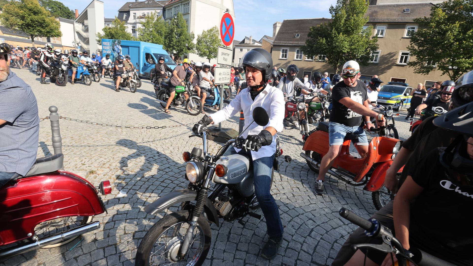 Ein amnn mit Motorradhelm sitzt auf einem Moped.