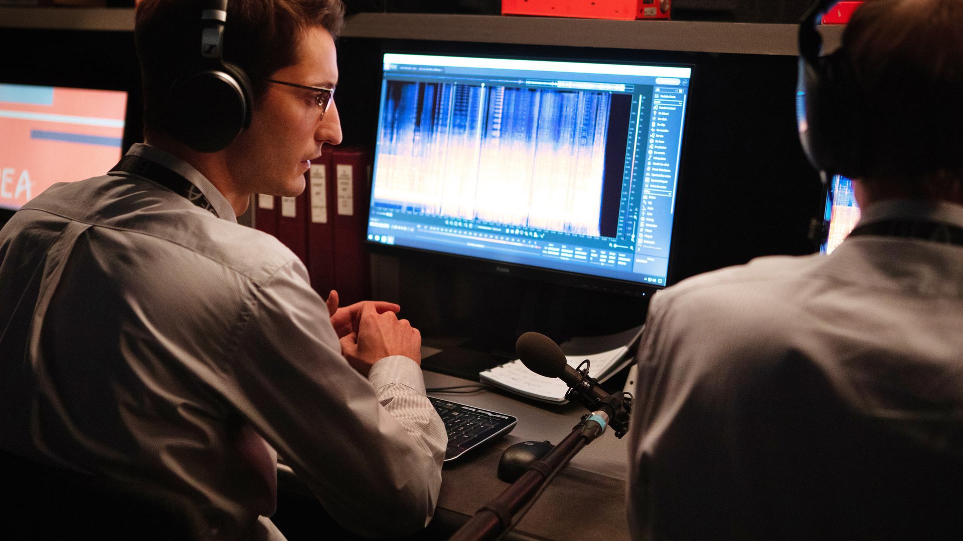Mathieu (Pierre Niney) sitzt mit Kopfhörern und halb abgewandt von der Kamera vor einem Computerbildschirm, auf dem Grafiken einer Tonaufnahme zu sehen sind. Neben ihm sitzt, nicht vollständig sichtbar, ein männlicher Kollege, der ebenfalls Kopfhörer trägt.