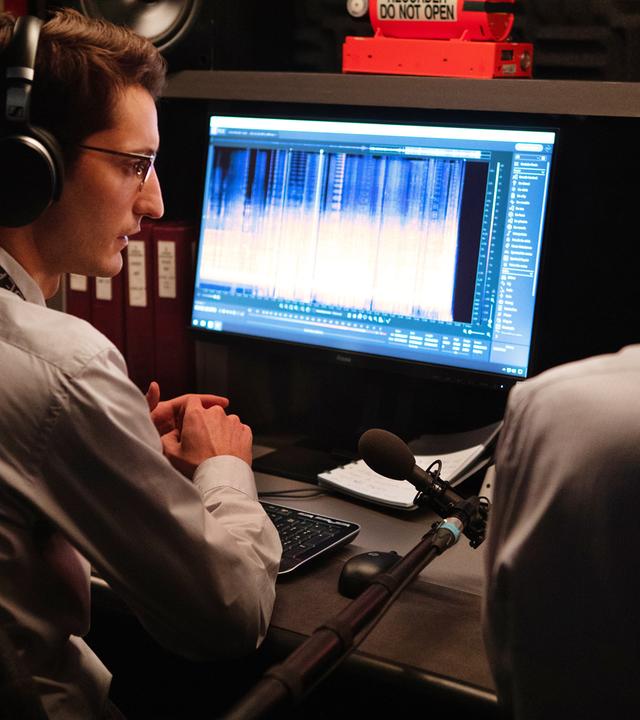 Mathieu (Pierre Niney) sitzt mit Kopfhörern und halb abgewandt von der Kamera vor einem Computerbildschirm, auf dem Grafiken einer Tonaufnahme zu sehen sind. Neben ihm sitzt, nicht vollständig sichtbar, ein männlicher Kollege, der ebenfalls Kopfhörer trägt.