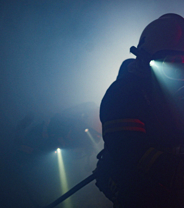 Stromtechniker mit Schutzhelm rollt in Dunkelheit und Nebel Kabeltrommel auf