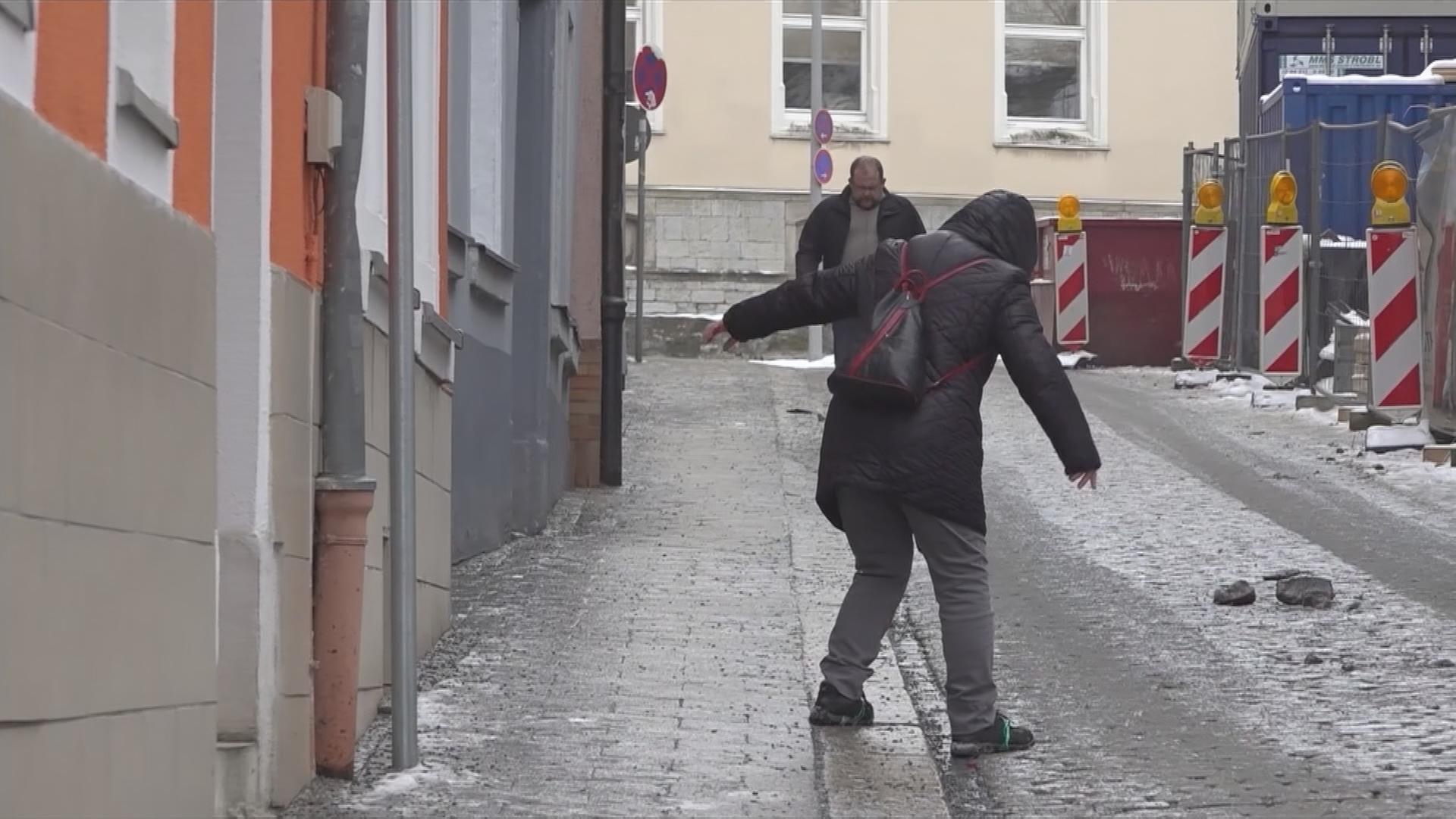 Frau geht bei Glatteis vom Fußweg auf die Straße
