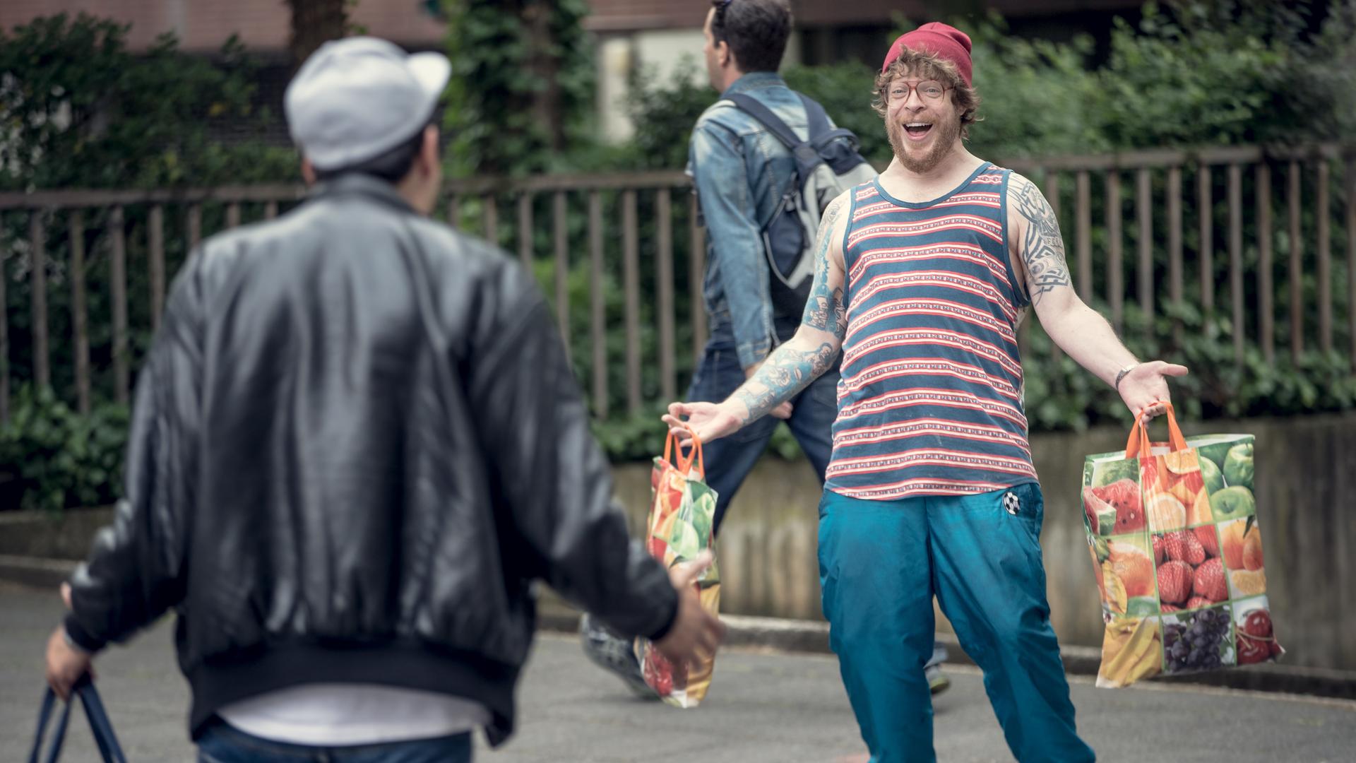 Sol und Hardy begrüßen sich auf der Straße, während sie Einkaufstüten tragen.
