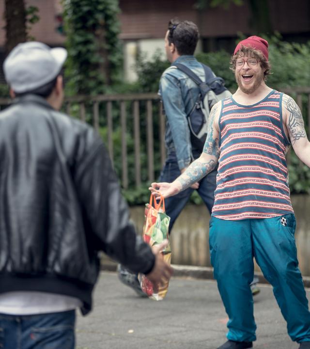 Sol und Hardy begrüßen sich auf der Straße, während sie Einkaufstüten tragen.