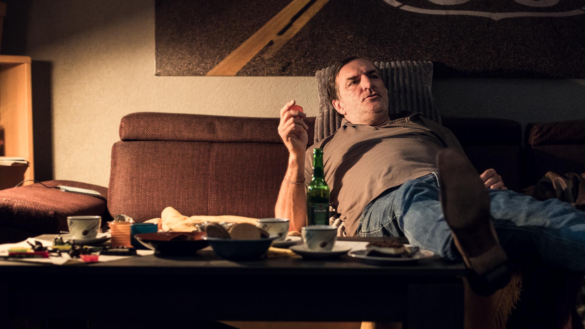 Ein Mann mittleren Alters liegt lustlos auf der Couch, ein Bein auf dem Kaffeetisch abgelegt.