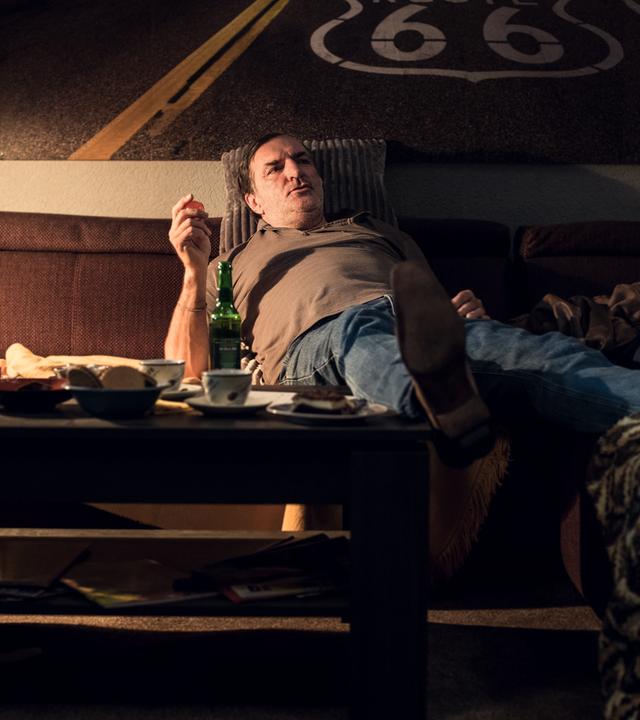 Ein Mann mittleren Alters liegt lustlos auf der Couch, ein Bein auf dem Kaffeetisch abgelegt.