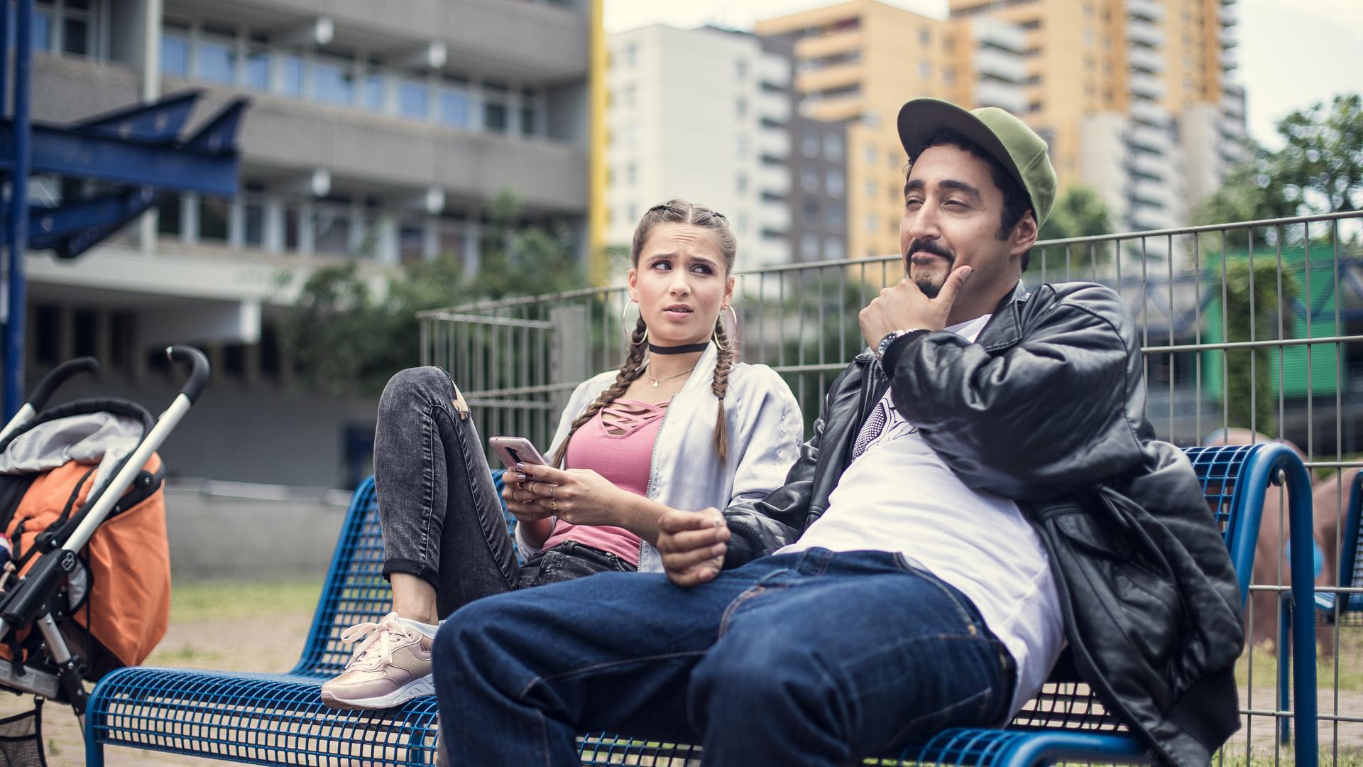 Sol und Jessica sitzen gemeinsam auf einer Bank im Hof des Blocks.
