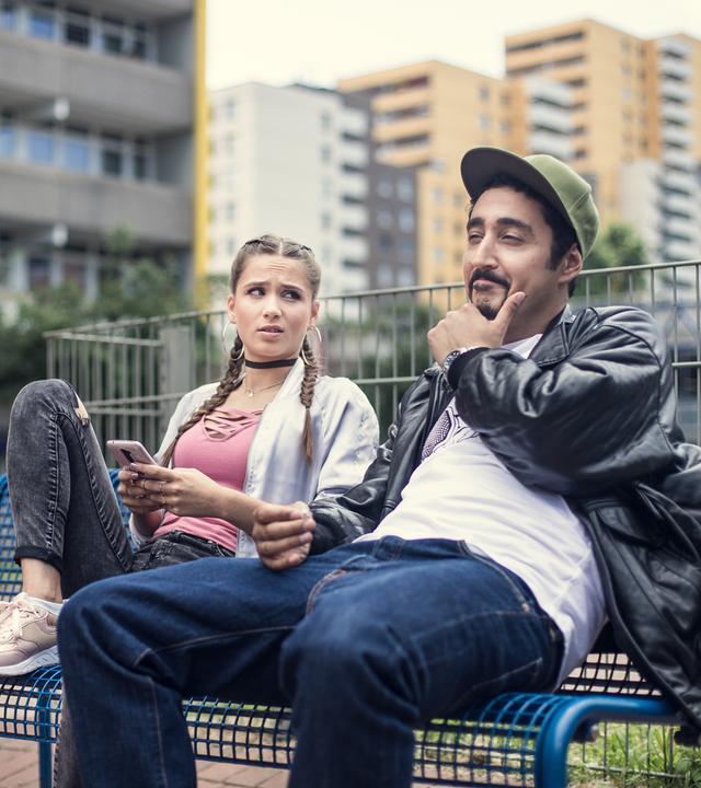 Sol und Jessica sitzen gemeinsam auf einer Bank im Hof des Blocks.