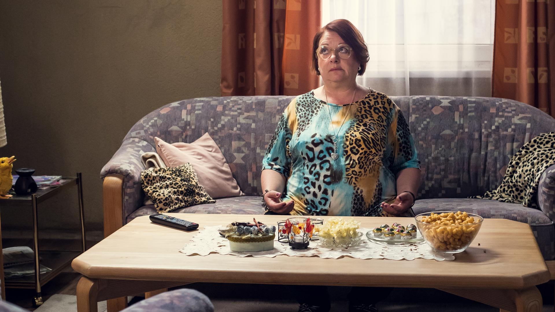 Hella sitzt in einem T-Shirt mit Leopardenmuster auf ihrer Couch.