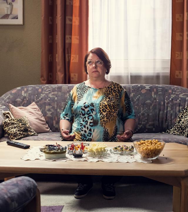 Hella sitzt in einem T-Shirt mit Leopardenmuster auf ihrer Couch.