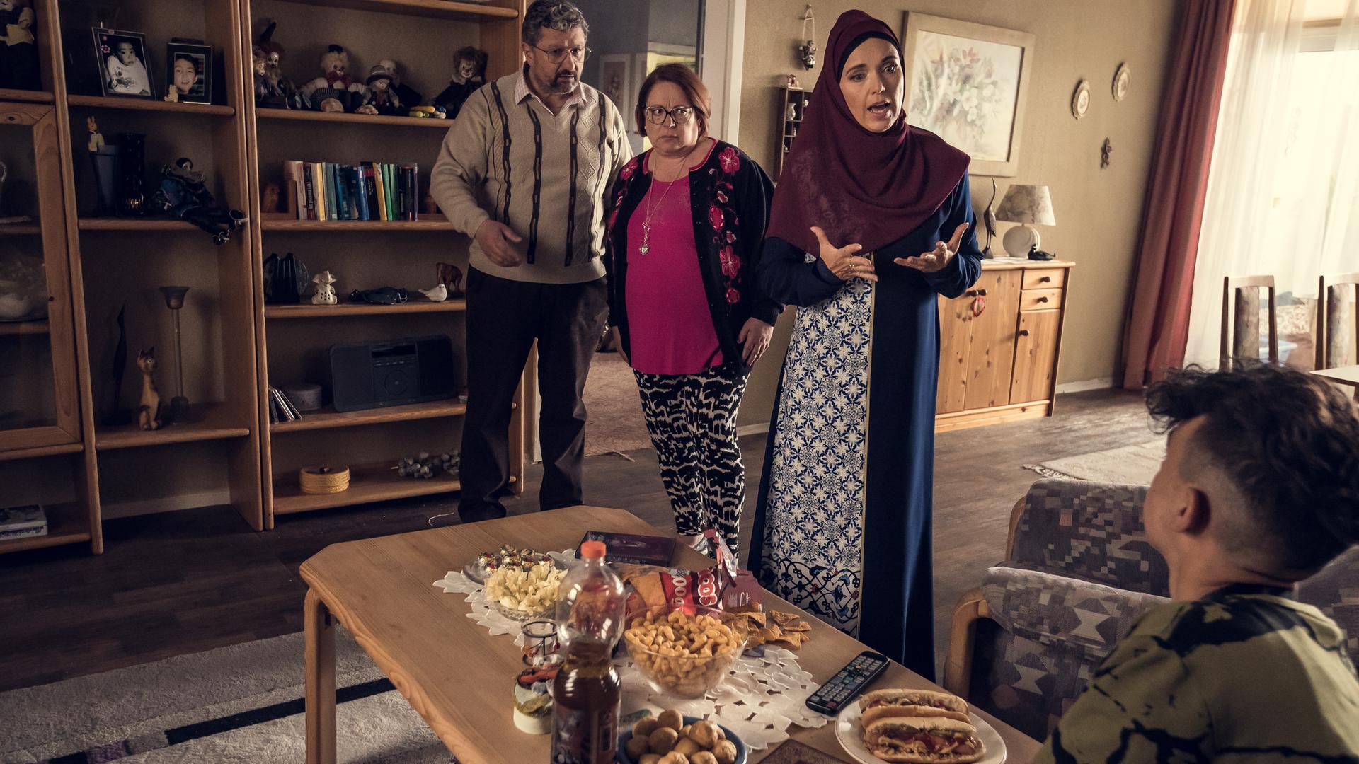 In einem altmodisch eingerichteten Wohnzimmer stehen drei ältere Familienmitglieder und schauen aufgebracht auf einen Jungen hinab, der auf der Couch sitzt.