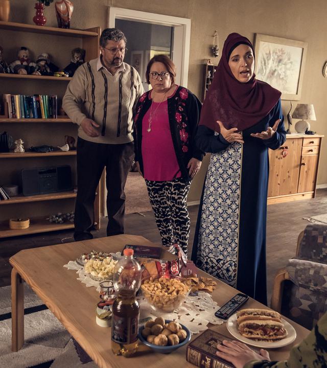 In einem altmodisch eingerichteten Wohnzimmer stehen drei ältere Familienmitglieder und schauen aufgebracht auf einen Jungen hinab, der auf der Couch sitzt.