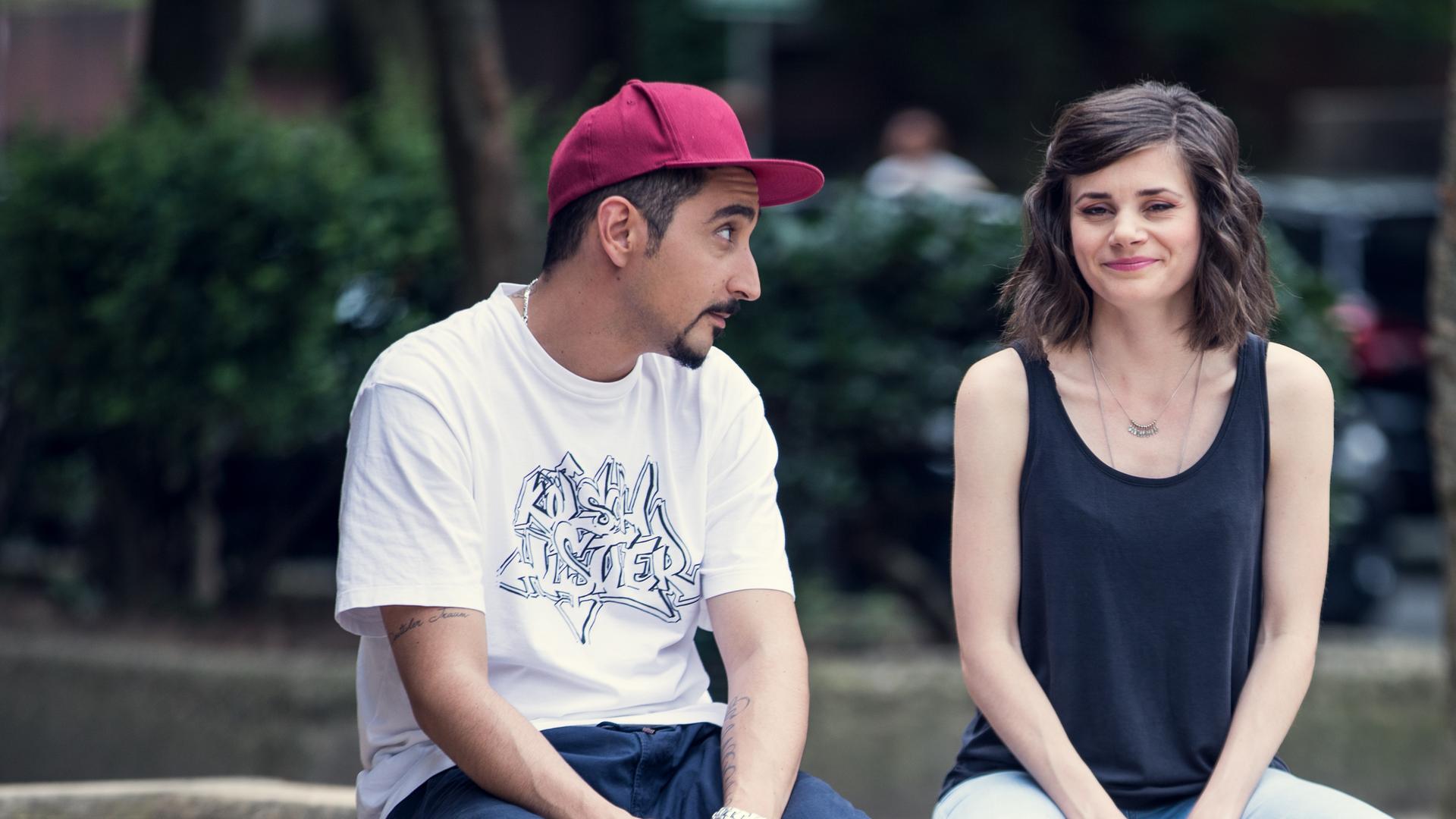 Sol und Jessica sitzen auf dem Rand eines hölzernen Blumenbeetes im Hof.