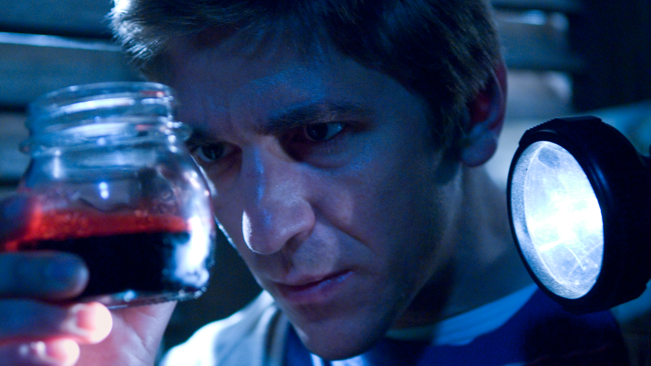 Fritz untersucht ein Glas in dem eine rote Flüssigkeit ist.