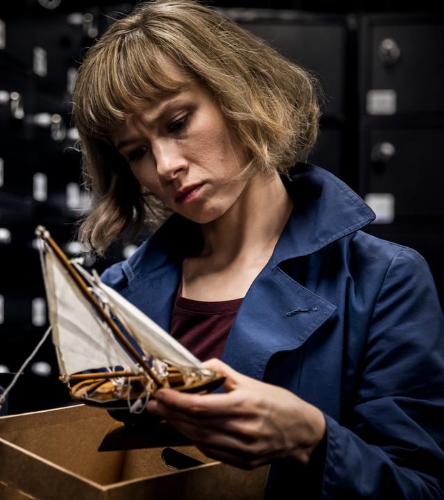 Eine Nahaufnahme von Doro Decker (Alina Levshin), die ein Spielzeugschiff in den Händen hält und inspiziert.