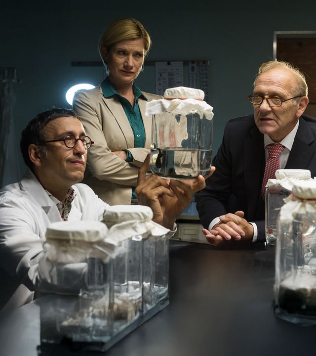 "SOKO Stuttgart - Blutsauger": Martina Seiffert (Astrid M. Fünderich) und Michael Kaiser (Karl Kranzkowski) sitzen in Jan Arnauds (Mike Zaka Sommerfeldt) Labor. Jan hält ein großes abgedecktes Glas in die Höhe darin befinden sich Wasser und Blutegel.