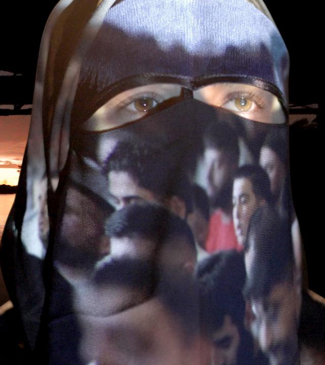 Eine Frau mit Burka, auf der Bilder projiziert werden, vor einer Flusslandschaft 