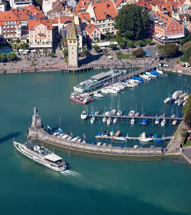 "ZDF.reportage: Bodensee - Urlauberlust und Anwohnerfrust": Luftaufnahme: Blick auf die Hafeneinfahrt von Lindau am Bodensee. Ein Ausflugsdampfer fährt gerade dort ein.