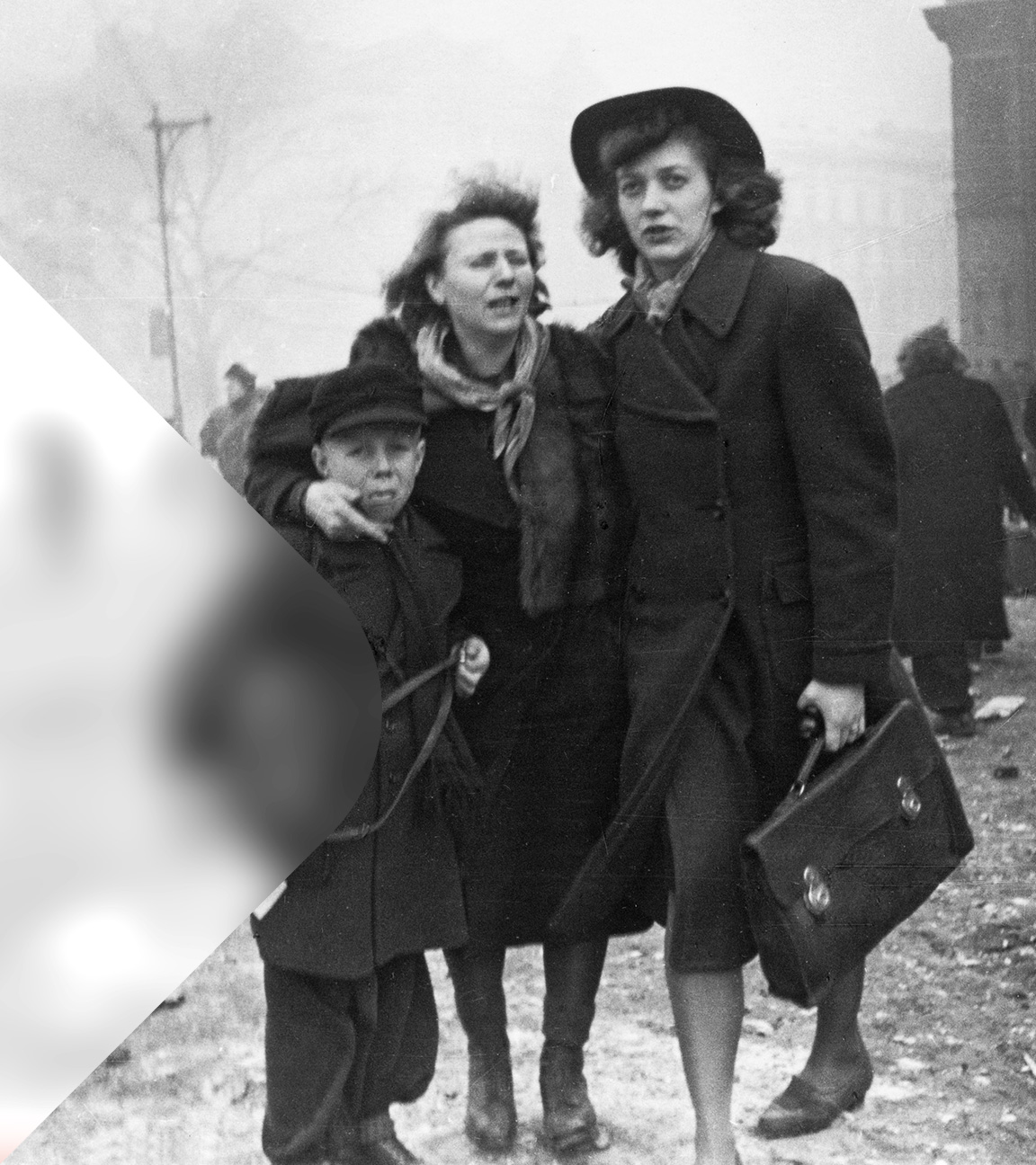 Schwarz-Weiß-Foto: Zwei Frauen und ein Junge stehen vor den Trümmern am Anhalter Bahnhof in Berlin nach einem Luftangriff im Februar 1945. Im Hintergrund laufen weitere Personen, Schutt liegt auf der Straße.