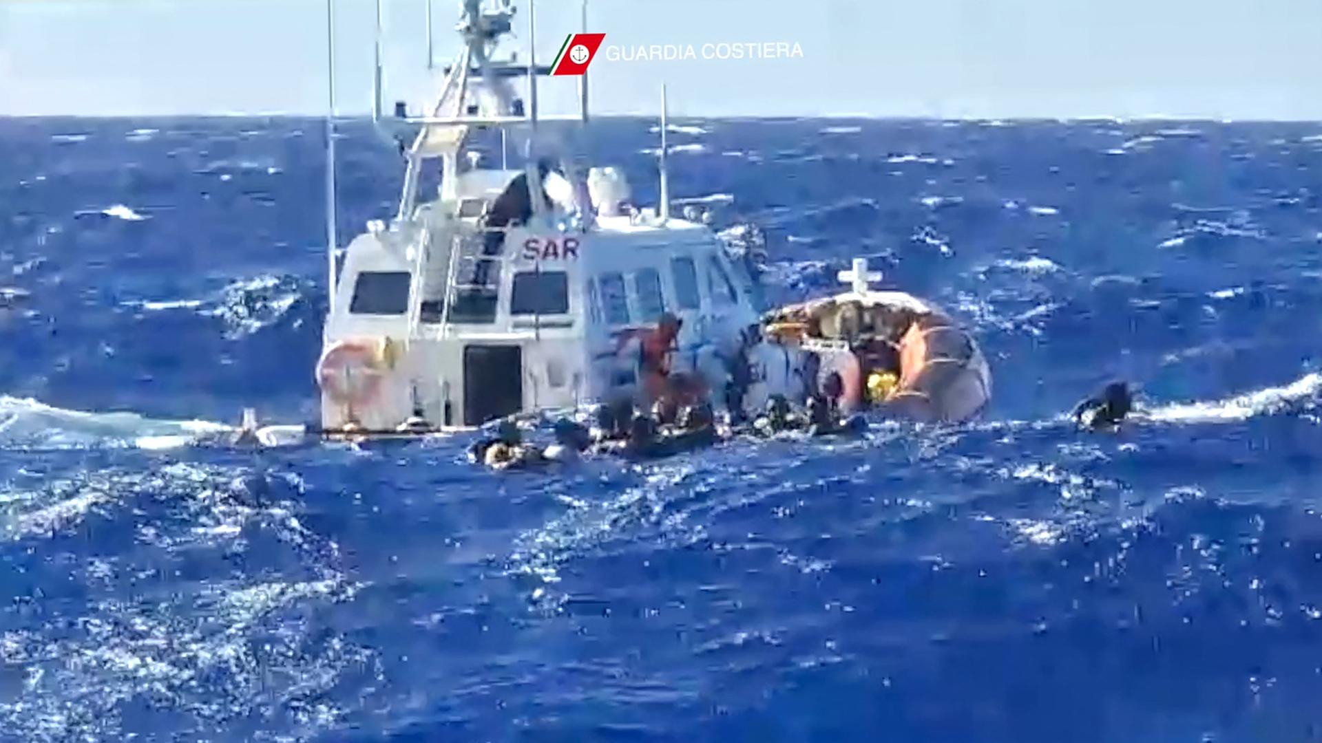 Bei hollem Wellengang versuchen Migranten von einem Boot auf ein Schiff der italienischen Küstenwache zu klettern.
