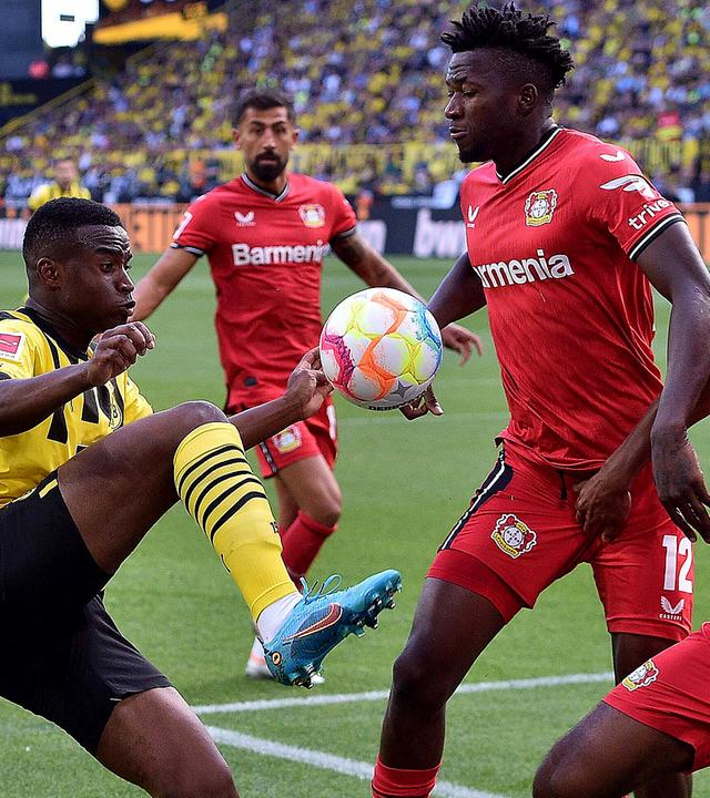 Youssoufa Moukoko (l, Dortmund) in Aktion gegen Jonathan Tah (r, Leverkusen) und Edmond Tapsoba (m, Leverkusen) am 06.08.2022.