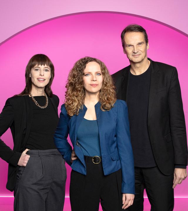 Auf dem Bild ist Sarah Bosetti mittig zu sehen. Links neben ihr steht die Historikerin Hedwig Richter, rechts neben ihr der Journalist und Autor Klaus Brinkbäumer. Der Hintergrund ist pink.