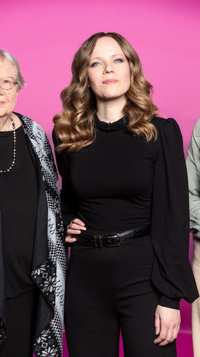 Auf dem Bild ist Sarah Bosetti mittig zu sehen. Links neben ihr steht Luise F Pusch. Auf der rechten Seite des Bildes ist Alicia Joe. Der Hintergrund ist rosa