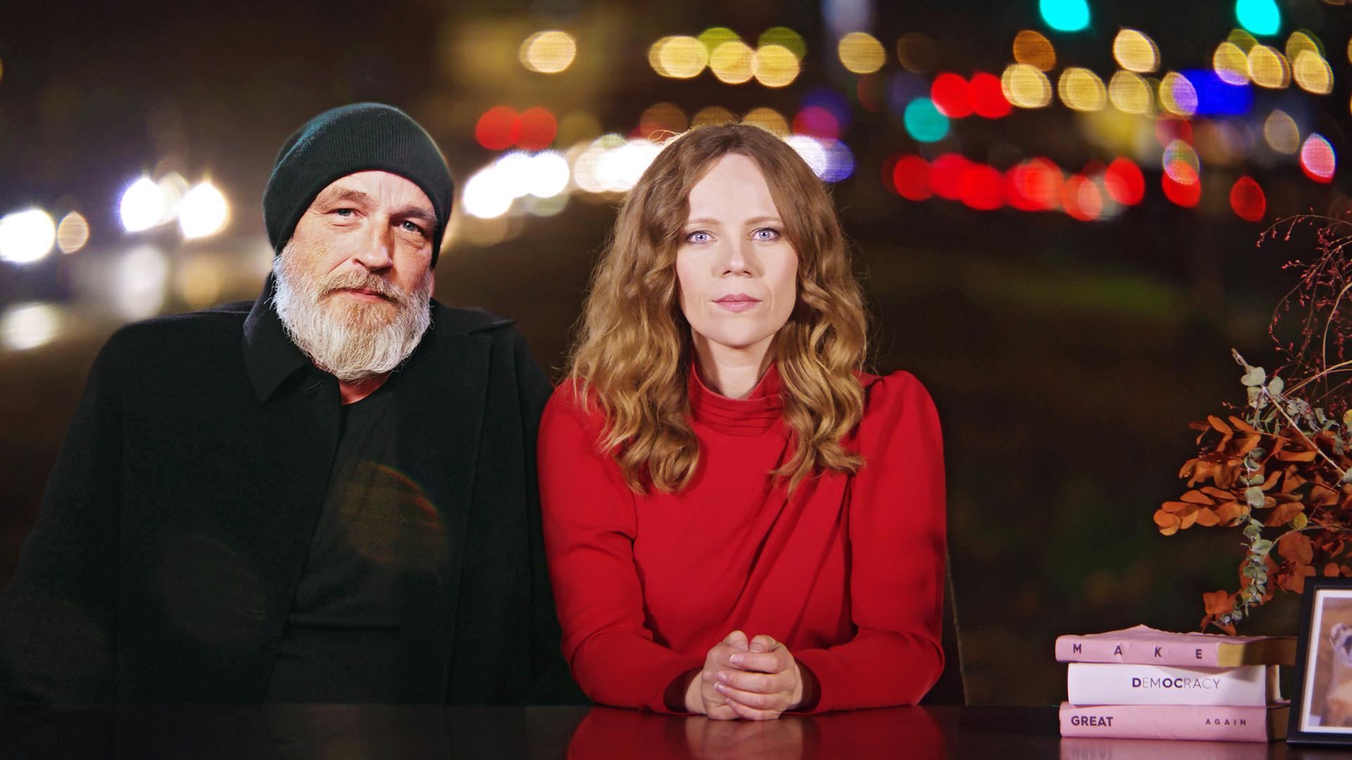 Auf dem Bild ist Sarah Bosetti auf der rechten Seite zu sehen. Links neben ihr sitzt Torsten Sträter. Beide sitzen hinter einen Schreibtisch.